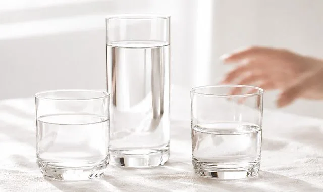Três copos de água fresca em diferentes tamanhos sobre uma mesa iluminada